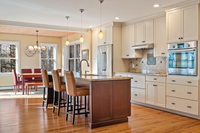 kitchen featuring an island with sink, stainless steel appliances, tasteful backsplash, pendant lighting, and sink