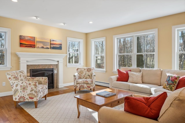 living room with a baseboard heating unit, a wealth of natural light, and light hardwood / wood-style flooring