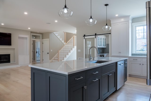 kitchen featuring sink, decorative light fixtures, light hardwood / wood-style flooring, a barn door, and a kitchen island with sink