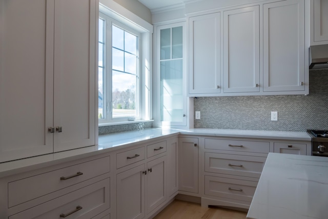 kitchen with decorative backsplash, white cabinetry, wall chimney range hood, and light stone countertops