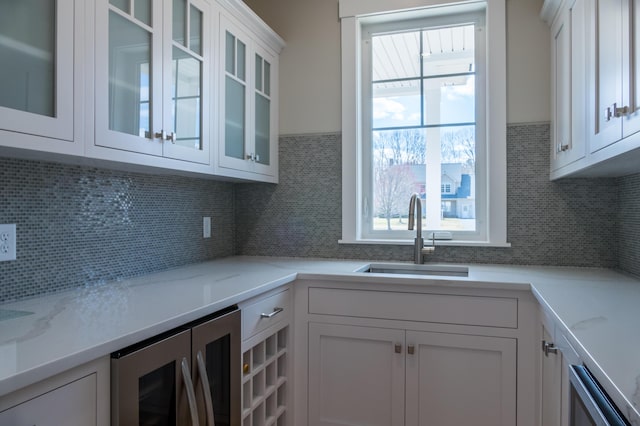 kitchen featuring white cabinets, wine cooler, light stone countertops, decorative backsplash, and sink