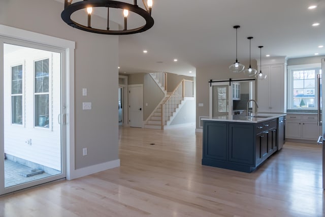 kitchen with a barn door, light hardwood / wood-style floors, an island with sink, sink, and decorative light fixtures