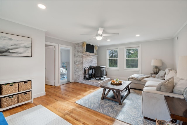 living room featuring hardwood / wood-style floors, ceiling fan, a wood stove, and crown molding