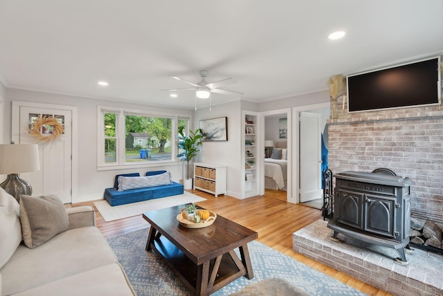 living room featuring ceiling fan, ornamental molding, a wood stove, and hardwood / wood-style flooring