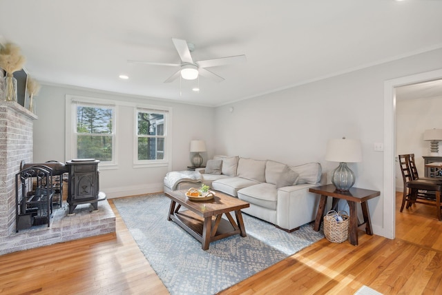 living room with ceiling fan, crown molding, a wood stove, and hardwood / wood-style flooring