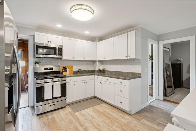 kitchen with stainless steel appliances, light hardwood / wood-style floors, decorative backsplash, white cabinets, and sink