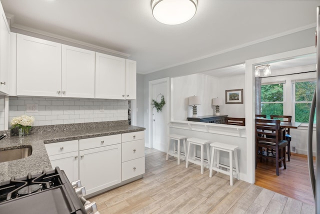 kitchen with light hardwood / wood-style flooring, white cabinetry, dark stone countertops, and backsplash