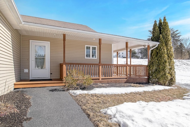 snow covered property entrance featuring a porch and roof with shingles