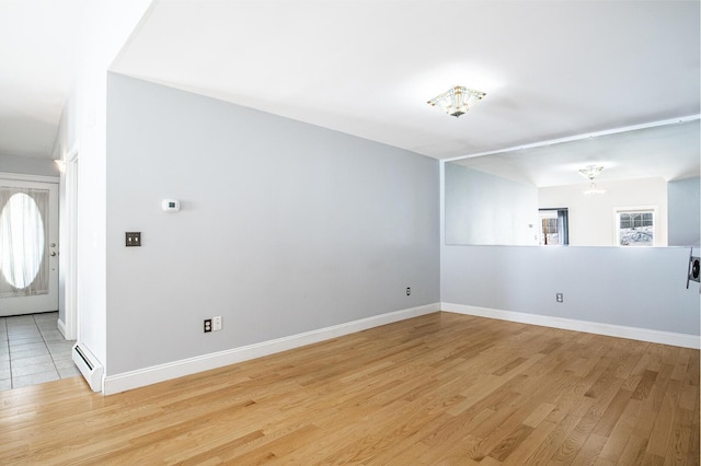 spare room with a chandelier, baseboards, light wood finished floors, and a baseboard radiator