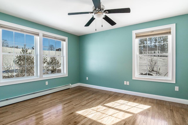 empty room featuring a ceiling fan, a baseboard heating unit, baseboards, and wood finished floors