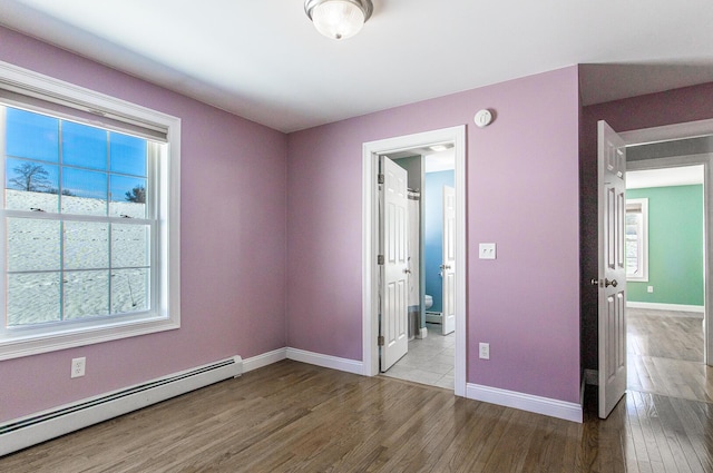 unfurnished bedroom featuring wood finished floors, baseboards, baseboard heating, and connected bathroom