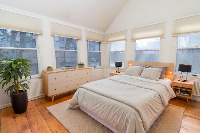 bedroom with high vaulted ceiling, radiator heating unit, and light hardwood / wood-style flooring