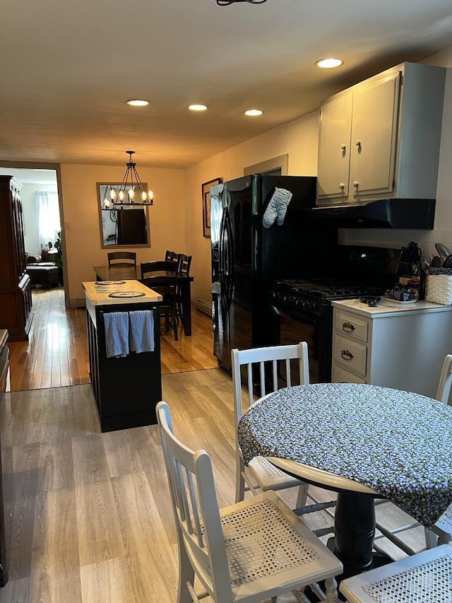 kitchen with black gas stove, decorative light fixtures, light wood-type flooring, a center island, and an inviting chandelier