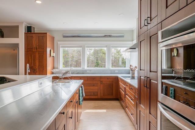 kitchen with stainless steel counters, brown cabinetry, appliances with stainless steel finishes, wall chimney range hood, and ornamental molding