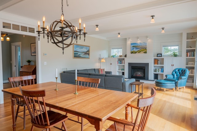 dining area with light wood-style flooring, a fireplace with raised hearth, built in shelves, a chandelier, and beam ceiling