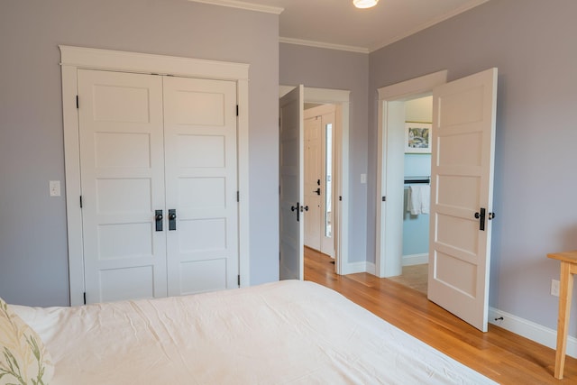 bedroom featuring light wood-style floors, a closet, crown molding, and baseboards
