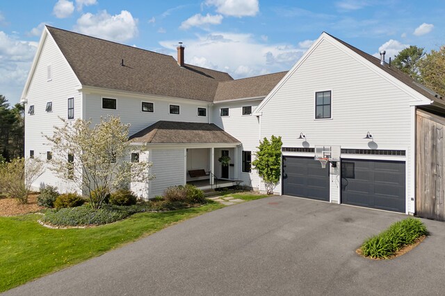 view of front of home featuring an attached garage, driveway, roof with shingles, and a chimney