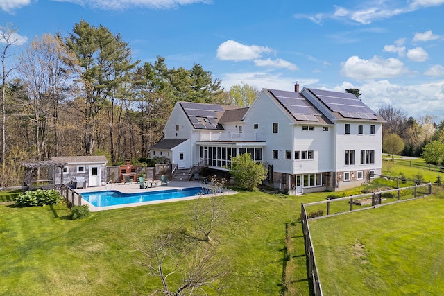 rear view of property featuring a sunroom, an outdoor structure, roof mounted solar panels, a wooden deck, and roof with shingles