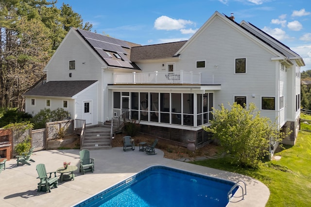 back of house featuring a balcony, a sunroom, a patio, an outdoor pool, and solar panels