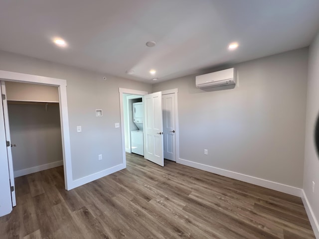 unfurnished bedroom featuring wood-type flooring, a walk in closet, a wall unit AC, and stacked washer and dryer