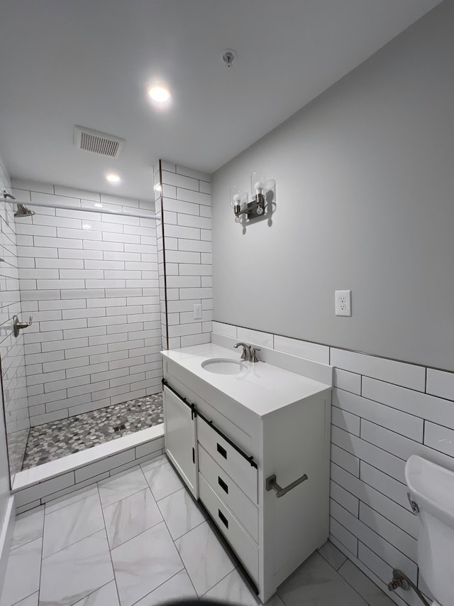 bathroom with tile walls, a tile shower, vanity, and toilet