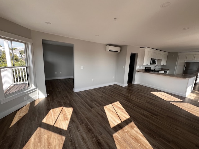 unfurnished living room featuring sink, dark wood-type flooring, and a wall mounted air conditioner