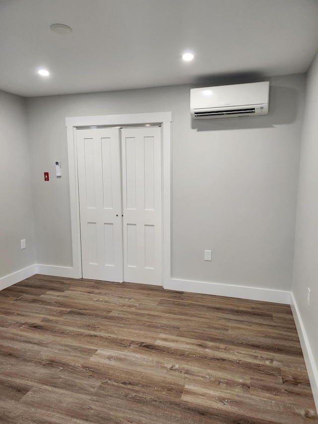 unfurnished bedroom with a wall mounted AC, a closet, and hardwood / wood-style floors