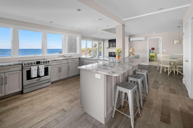 kitchen with a wall unit AC, a breakfast bar, gray cabinets, stainless steel electric range oven, and a water view