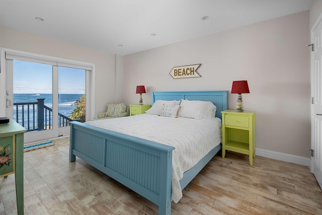 bedroom with access to exterior, light wood-type flooring, and a water view