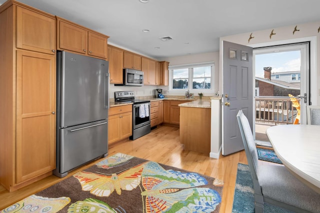 kitchen with stainless steel appliances, light wood-type flooring, and light stone counters