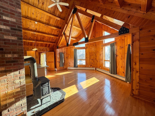 unfurnished living room with ceiling fan, beamed ceiling, a wood stove, baseboard heating, and wooden ceiling