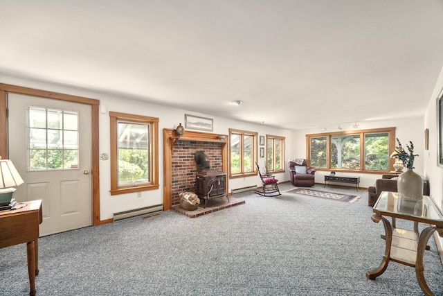 living room featuring baseboard heating, plenty of natural light, carpet floors, and a wood stove