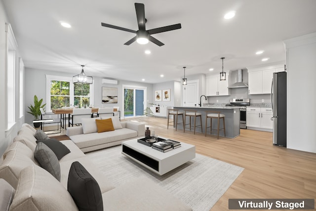 living room with light hardwood / wood-style floors, ceiling fan with notable chandelier, a wall mounted air conditioner, and sink