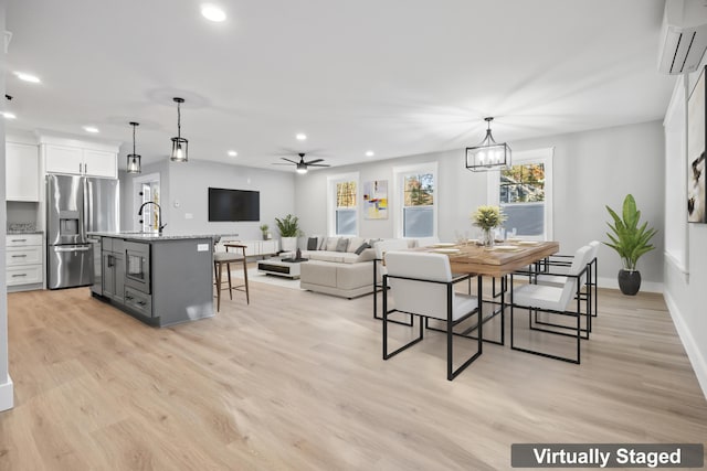 dining space featuring ceiling fan with notable chandelier, light hardwood / wood-style flooring, a wall mounted air conditioner, and sink