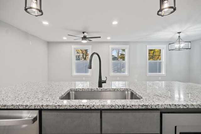 kitchen with sink, ceiling fan with notable chandelier, light stone counters, and hanging light fixtures