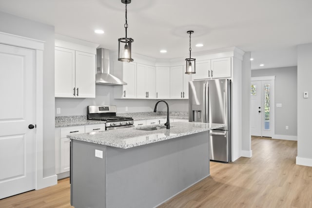 kitchen with stainless steel appliances, sink, wall chimney exhaust hood, light stone countertops, and a kitchen island with sink