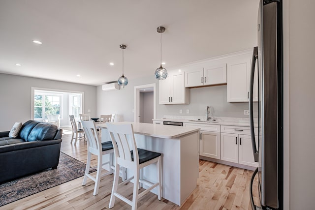 kitchen with decorative light fixtures, white cabinetry, stainless steel fridge, a kitchen island, and a breakfast bar