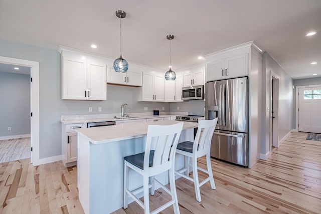 kitchen featuring decorative light fixtures, stainless steel appliances, light wood-type flooring, white cabinets, and sink