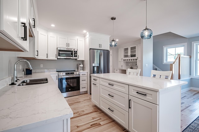 kitchen with pendant lighting, a kitchen island, white cabinetry, appliances with stainless steel finishes, and sink