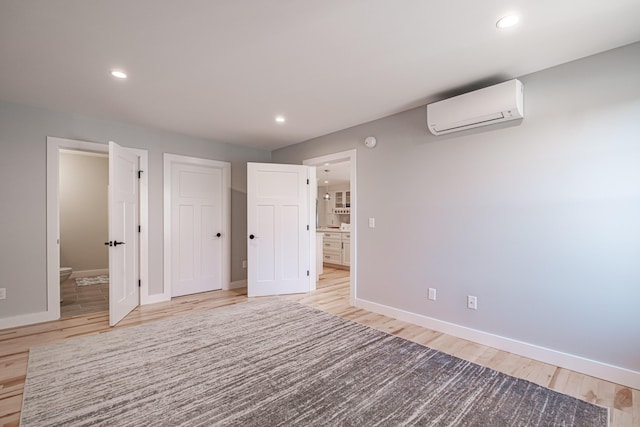 unfurnished bedroom with a wall unit AC, connected bathroom, and light wood-type flooring