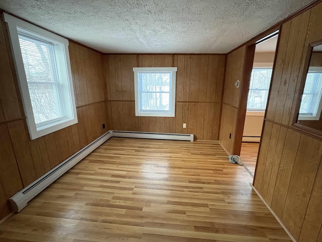 spare room featuring a baseboard radiator, wood walls, and light hardwood / wood-style flooring