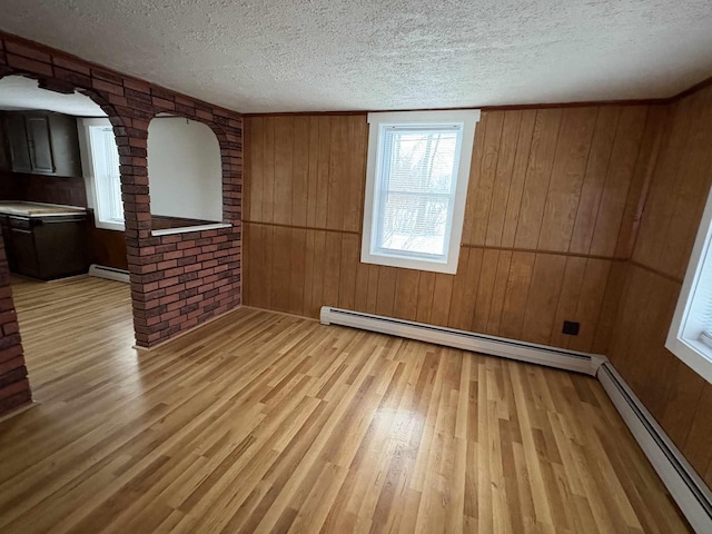 empty room featuring a textured ceiling, a baseboard radiator, and brick wall