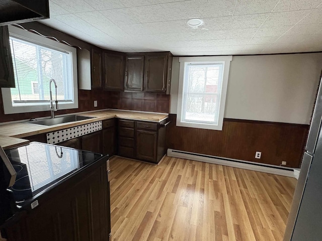 kitchen featuring a healthy amount of sunlight, wood walls, a baseboard heating unit, dark brown cabinets, and sink