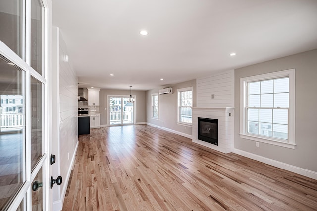 unfurnished living room featuring light wood-type flooring, an inviting chandelier, and an AC wall unit