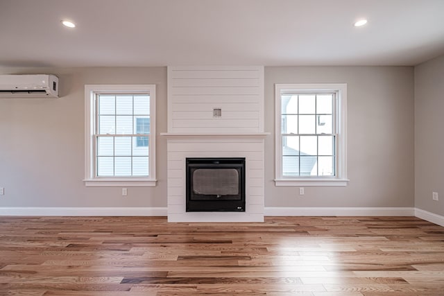 unfurnished living room featuring a large fireplace, an AC wall unit, light wood-type flooring, and a healthy amount of sunlight