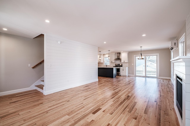 unfurnished living room featuring light wood-type flooring, a wall mounted air conditioner, a chandelier, and sink