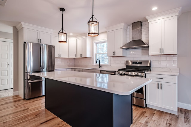 kitchen featuring white cabinets, appliances with stainless steel finishes, wall chimney exhaust hood, and pendant lighting