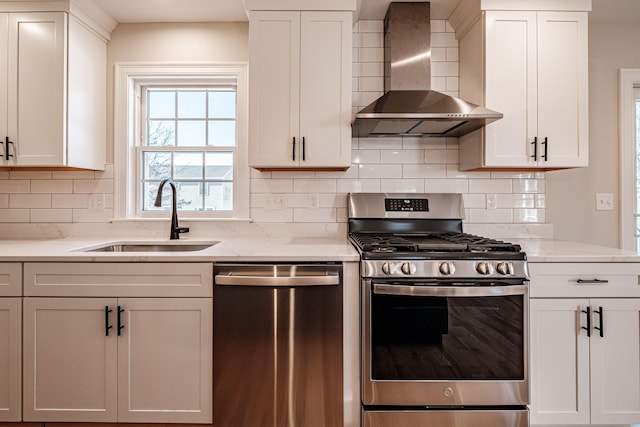 kitchen featuring appliances with stainless steel finishes, white cabinetry, wall chimney range hood, and sink