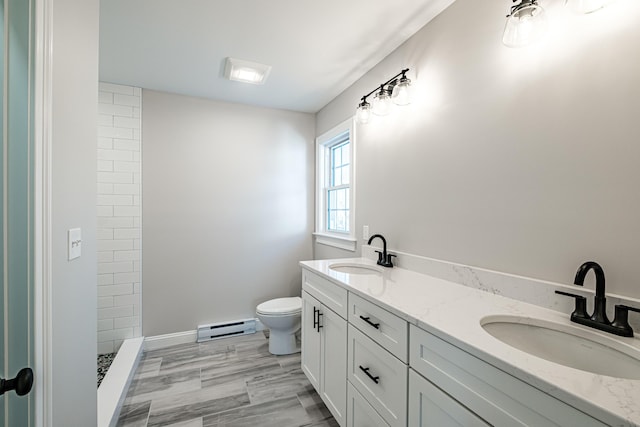 bathroom with tiled shower, toilet, vanity, and a baseboard heating unit