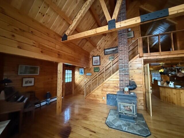 55 Brown Rd, Oakfield, ME 04763 - living room featuring hardwood / wood-style flooring, wood walls, wooden ceiling, beamed ceiling, and a wood stove